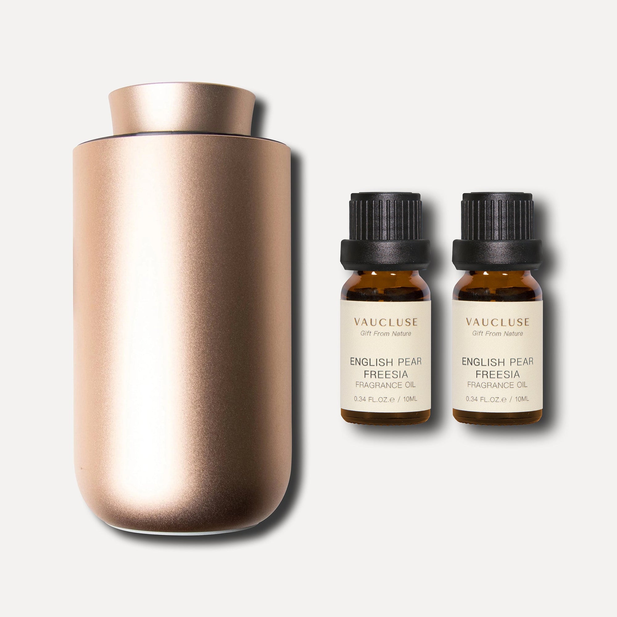 A minimalist rose gold waterless nebulizing aroma diffuser displayed next to two 10ml amber bottles of English pear and freesia essential oil.